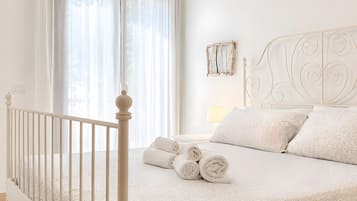 Un lit à baldaquin blanc avec des serviettes enroulées, une tête de lit blanche et un cadre photo fixé au mur.