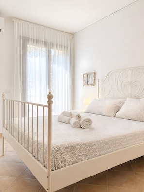 Una cama con dosel blanco, toallas enrolladas, cabecera blanca y un marco de fotos colgado en la pared.