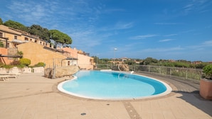 Una piscina con bordo curvo, circondata da un solarium piastrellato e recintata da una staccionata.