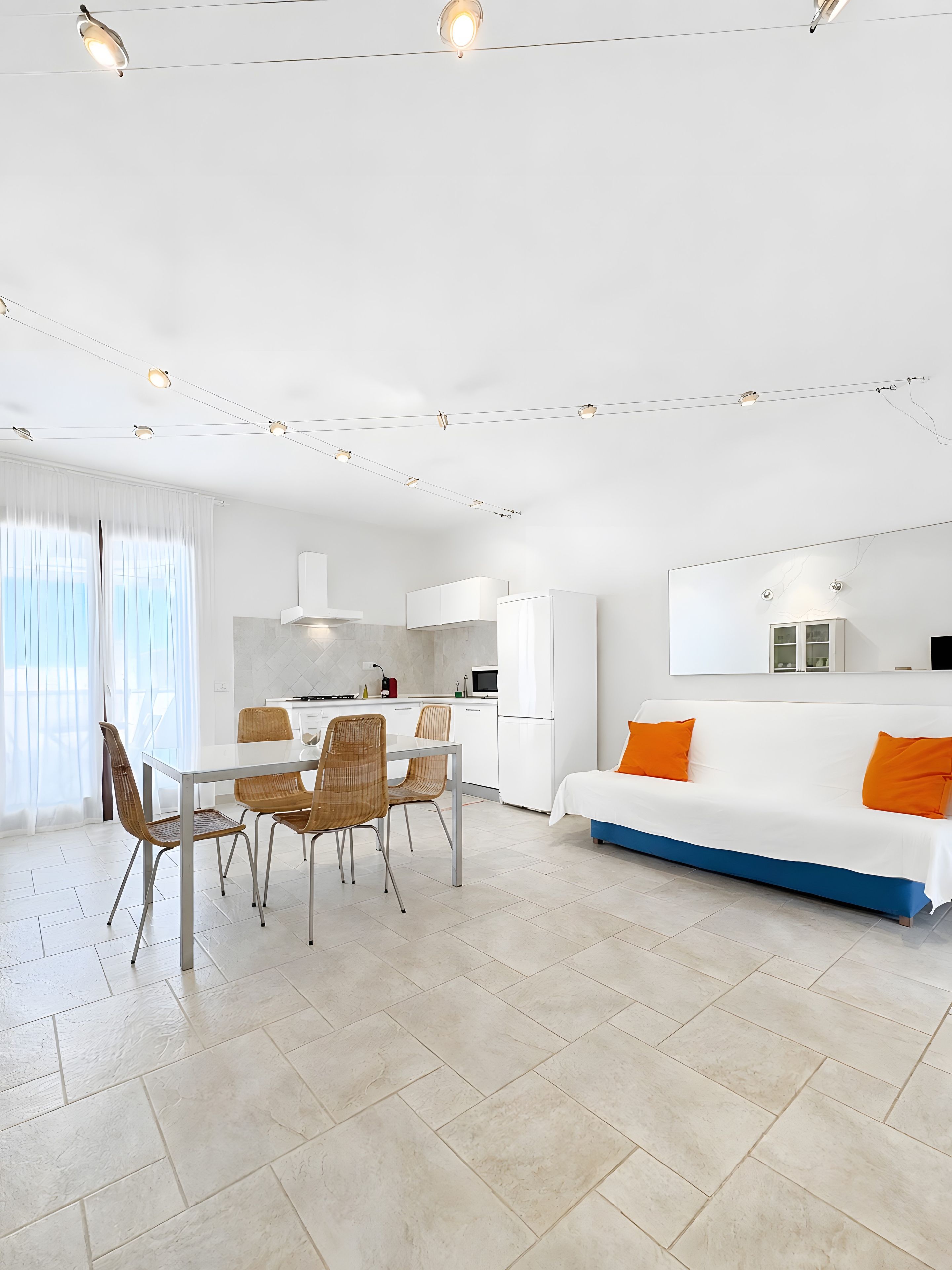 Un espacio de sala de estar moderno y bien iluminado, con una mesa de comedor, sillas y un sofá con cojines naranja.