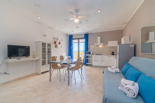 A modern kitchen with a dining area, a TV, and a sofa with towels.