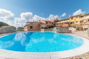 A swimming pool with a wooden deck, a building with a tiled roof, and a clear blue sky.