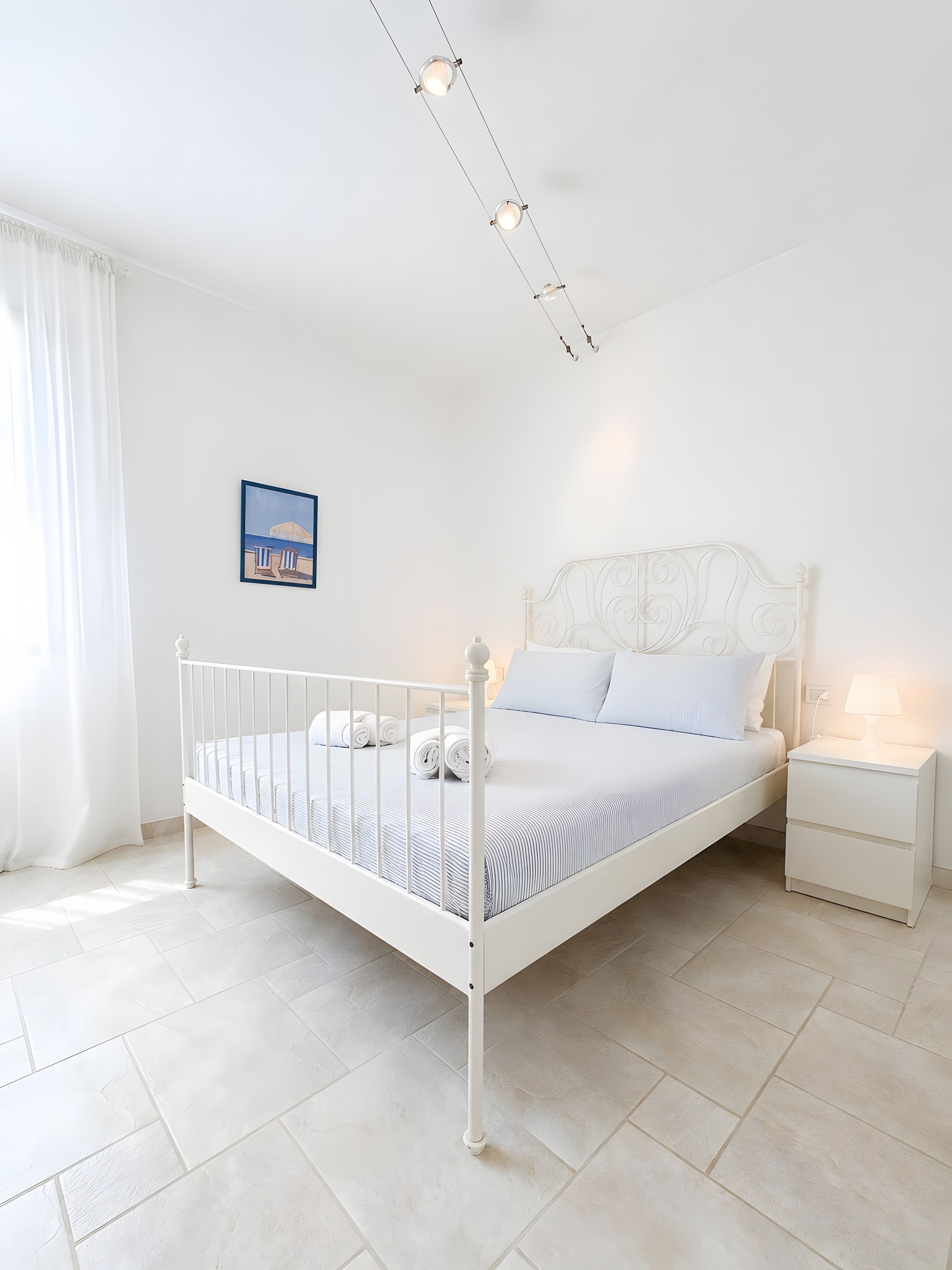 Un dormitorio blanco con una cama individual, una mesita de noche y un cuadro colgado en la pared.