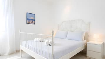 Un dormitorio blanco con una cama individual, una mesita de noche y un cuadro colgado en la pared.