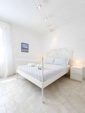 Une chambre à coucher blanche avec un lit simple, une table de chevet et un tableau accroché au mur.
