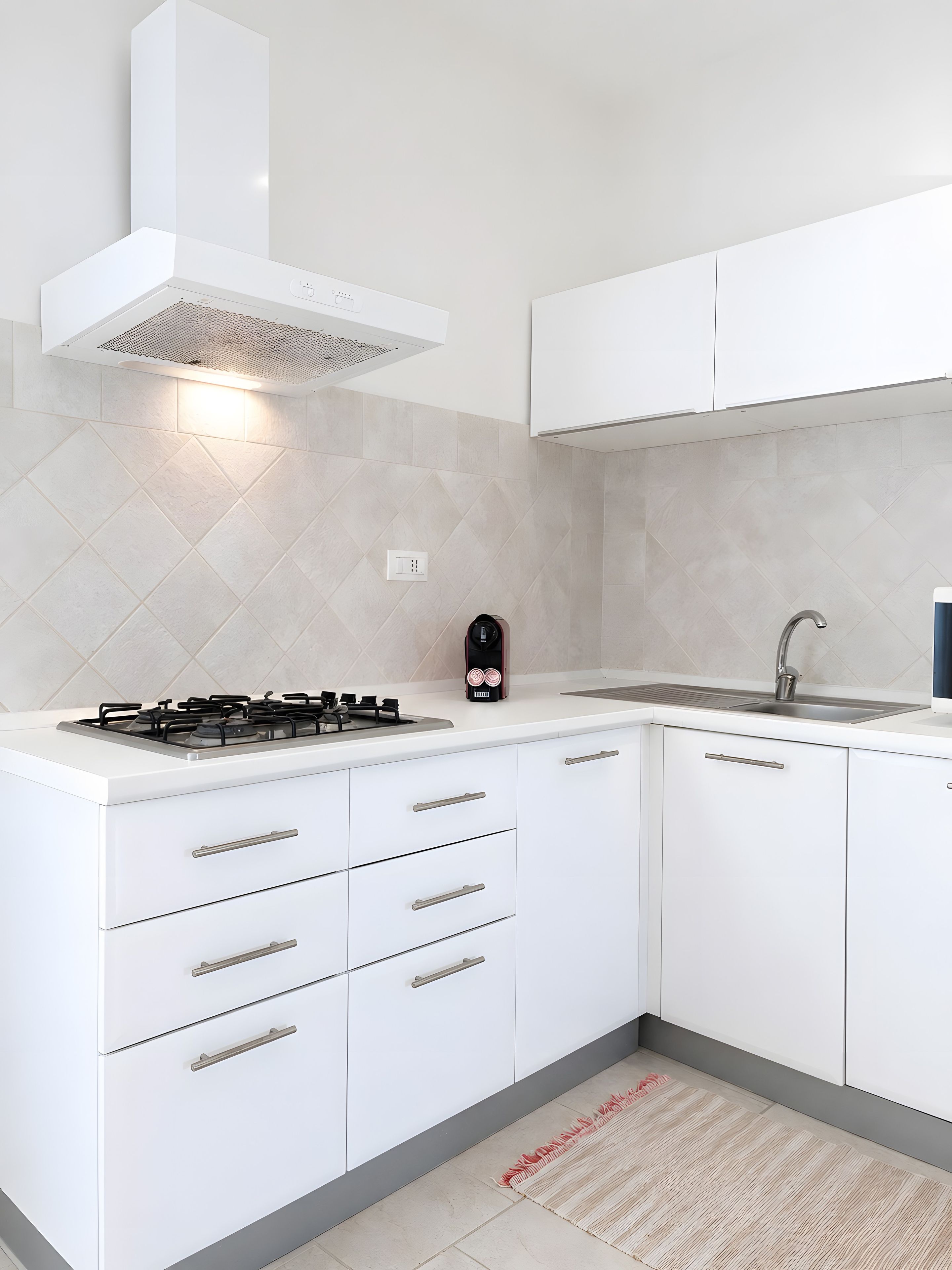 Una cocina moderna con estufa a gas, campana extractora integrada, pileta de acero inoxidable y alacenas blancas.
