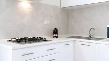 Una cocina moderna con estufa a gas, campana extractora integrada, pileta de acero inoxidable y alacenas blancas.