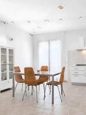 Un espace repas moderne avec une table en verre, des chaises en osier et un buffet blanc doté de portes en verre.