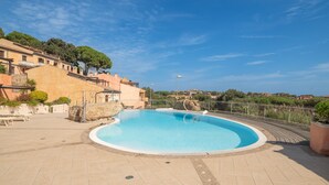 A swimming pool with a curved edge, surrounded by a tiled deck, and a fence enclosing the area. - Vacation Apartment "B 104 Puntavilla Mare" – Sea View (la maddalena)