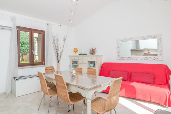 A dining area with a table and chairs, a red sofa, a white cabinet, and a mirror on the wall.