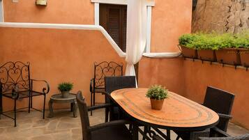 Een buitenpatio met een ronde tafel, rieten stoelen, potplanten en een stenen vloer.