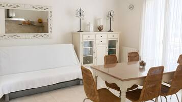 Een kamer met een bed, een eettafel met stoelen, een kast en een spiegel aan de muur.