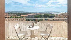 A balcony with two chairs and a table, overlooking a coastal town with buildings and mountains in the distance. - Vacation Apartment "B 104 Puntavilla Mare" – Sea View (la maddalena)