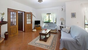 A living room with a sofa, a coffee table, a TV, and a door leading to another room. - Pet-friendly Casa da Alfarrobeira with Pool & Wi-Fi (Loulé)