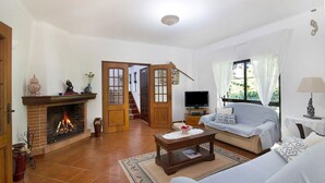 A living room with a fireplace, sofa, television, and a view of the outdoors. - Pet-friendly Casa da Alfarrobeira with Pool & Wi-Fi (Loulé)
