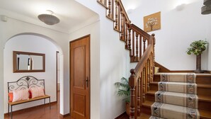 A staircase with wooden balusters, a bench with striped cushions, a wooden door, and a potted plant. - Pet-friendly Casa da Alfarrobeira with Pool & Wi-Fi (Loulé)