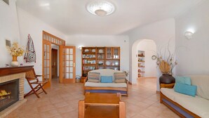 Ein Wohnzimmer mit Kamin, Sofa, Couchtisch, Bücherregal und Essbereich.