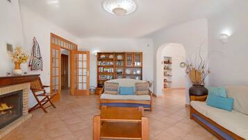 A living room with a fireplace, sofa, coffee table, bookshelf, and a dining area.
