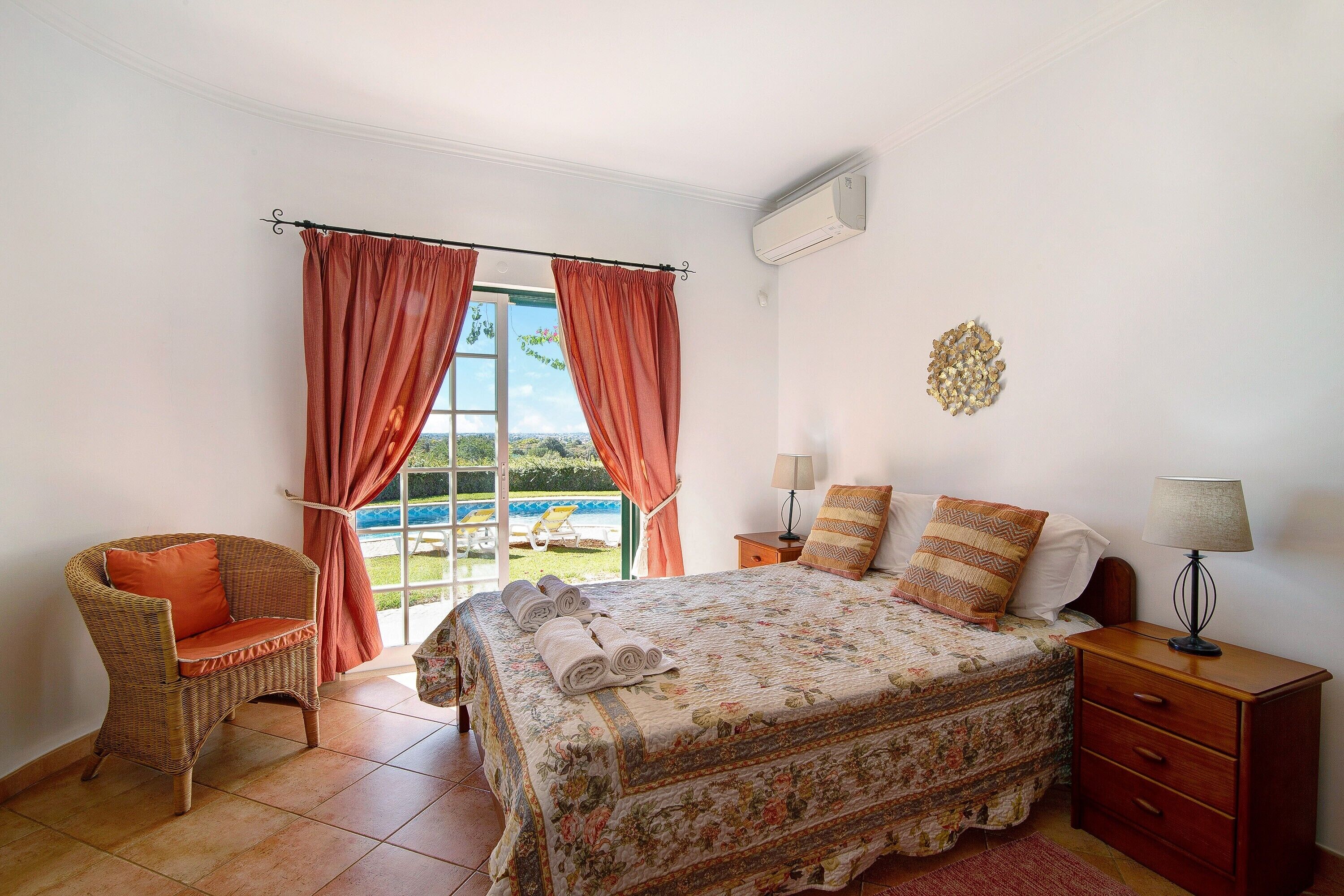 A bedroom with a bed, a chair, a nightstand, and a window with curtains.