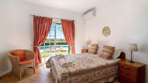 Ein Schlafzimmer mit einem Bett, einem Sessel, einem Nachttisch und einem Fenster mit Vorhängen.