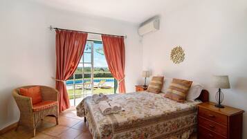 A bedroom with a bed, a chair, a nightstand, and a window with curtains.