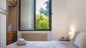 A bedroom with a bed, a window, a radiator, a nightstand, and a dresser.