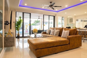 Relax in this inviting living room with a large sofa, ceiling fan, and a view of the outside through the large window.