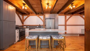 A kitchen with wooden beams, a central island, bar stools, and modern appliances. - RIVER! Hot tub, Movie theater, Sauna, Massage chair (Conway)