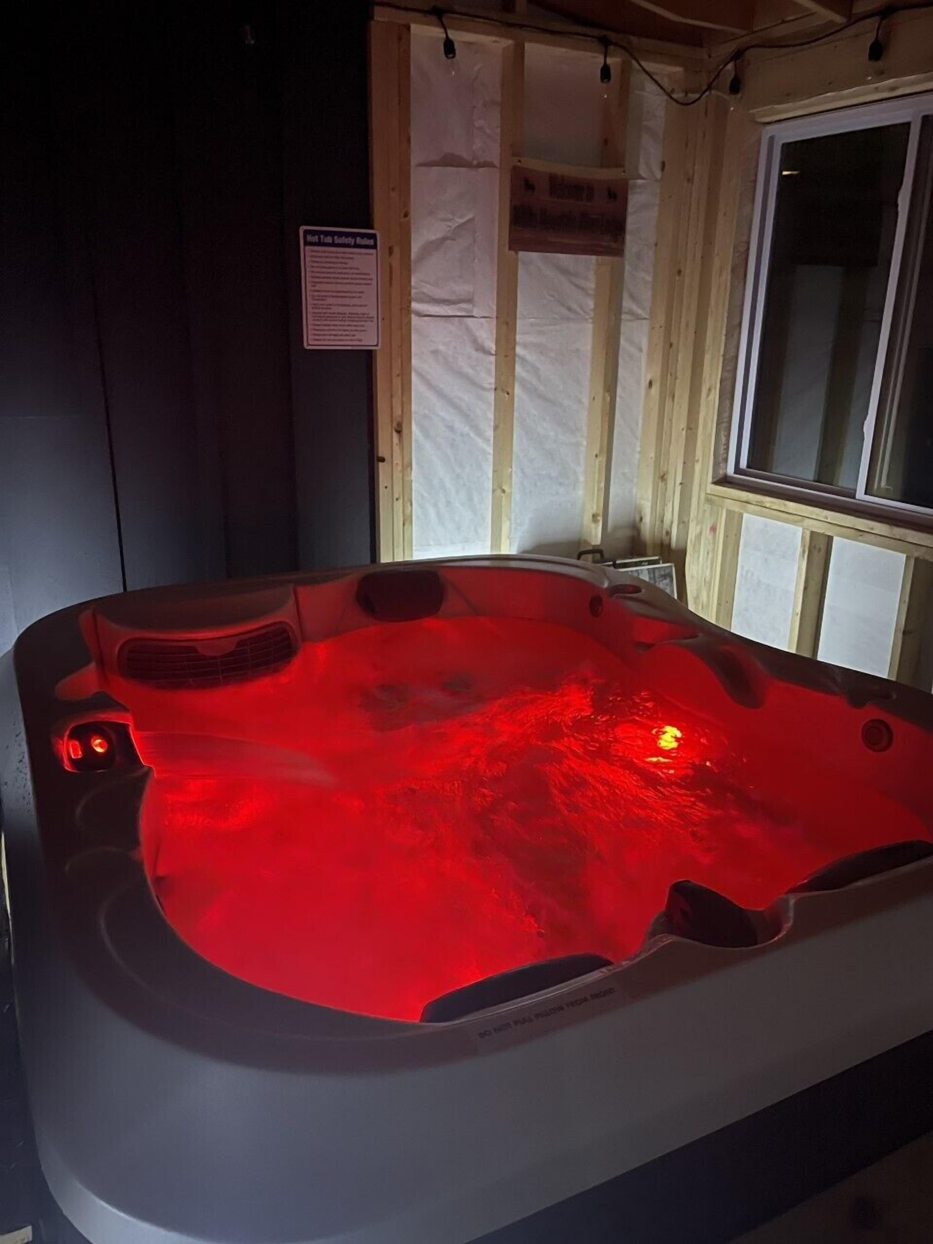 Un bain à remous éclairé d’une lumière rouge, entouré de murs en bois et doté d’une fenêtre.