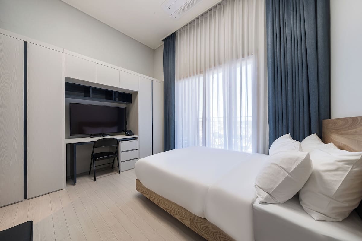 A modern hotel room with a large bed, a desk with a flat-screen TV, and a window with curtains.