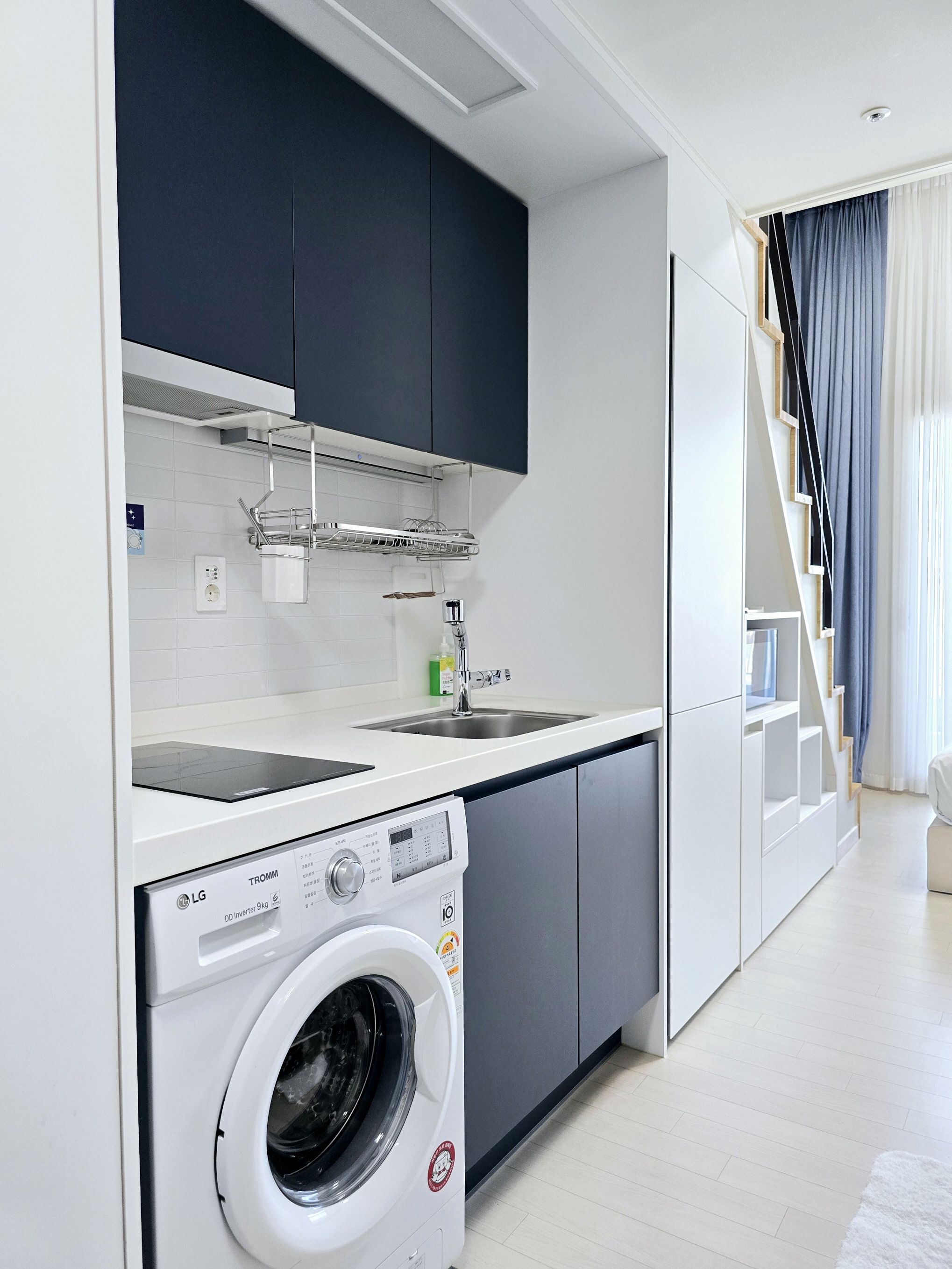 A modern kitchen with a built-in washing machine, a sink, and a staircase leading to an upper level.