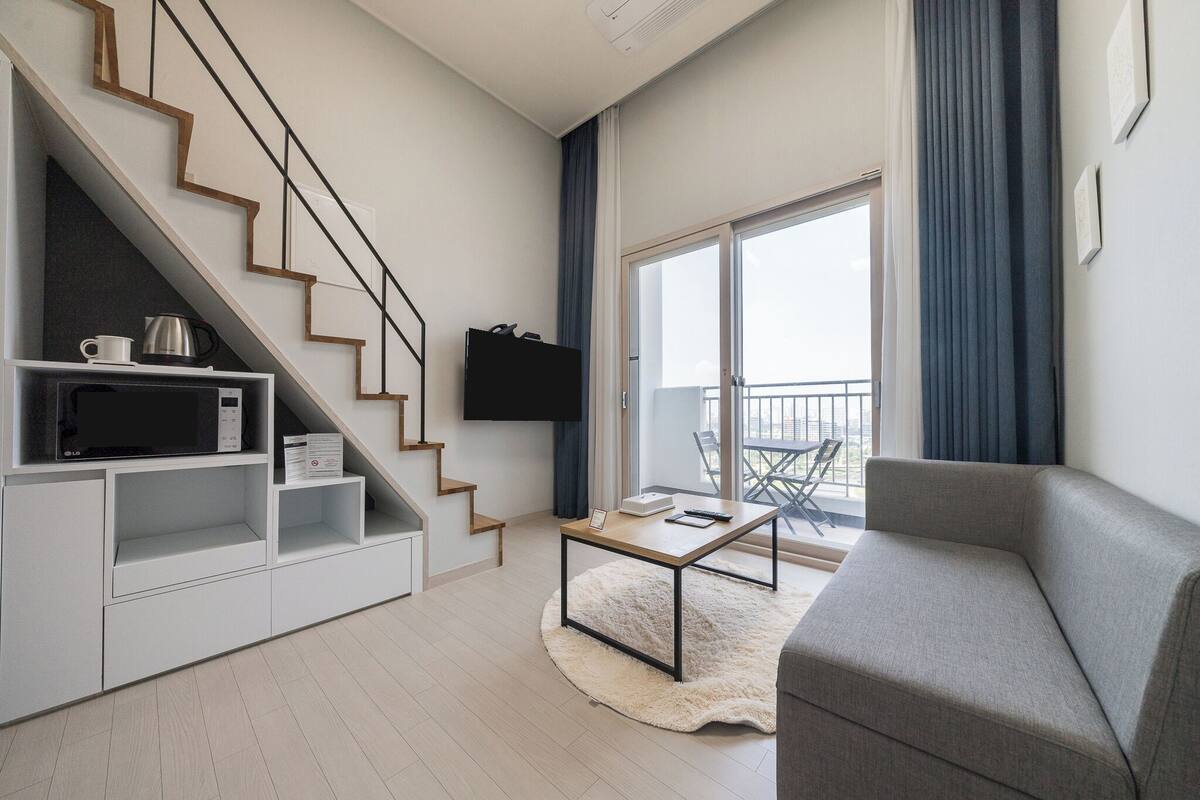 A modern living room with a staircase, a flat-screen TV, a coffee table, and a sofa.