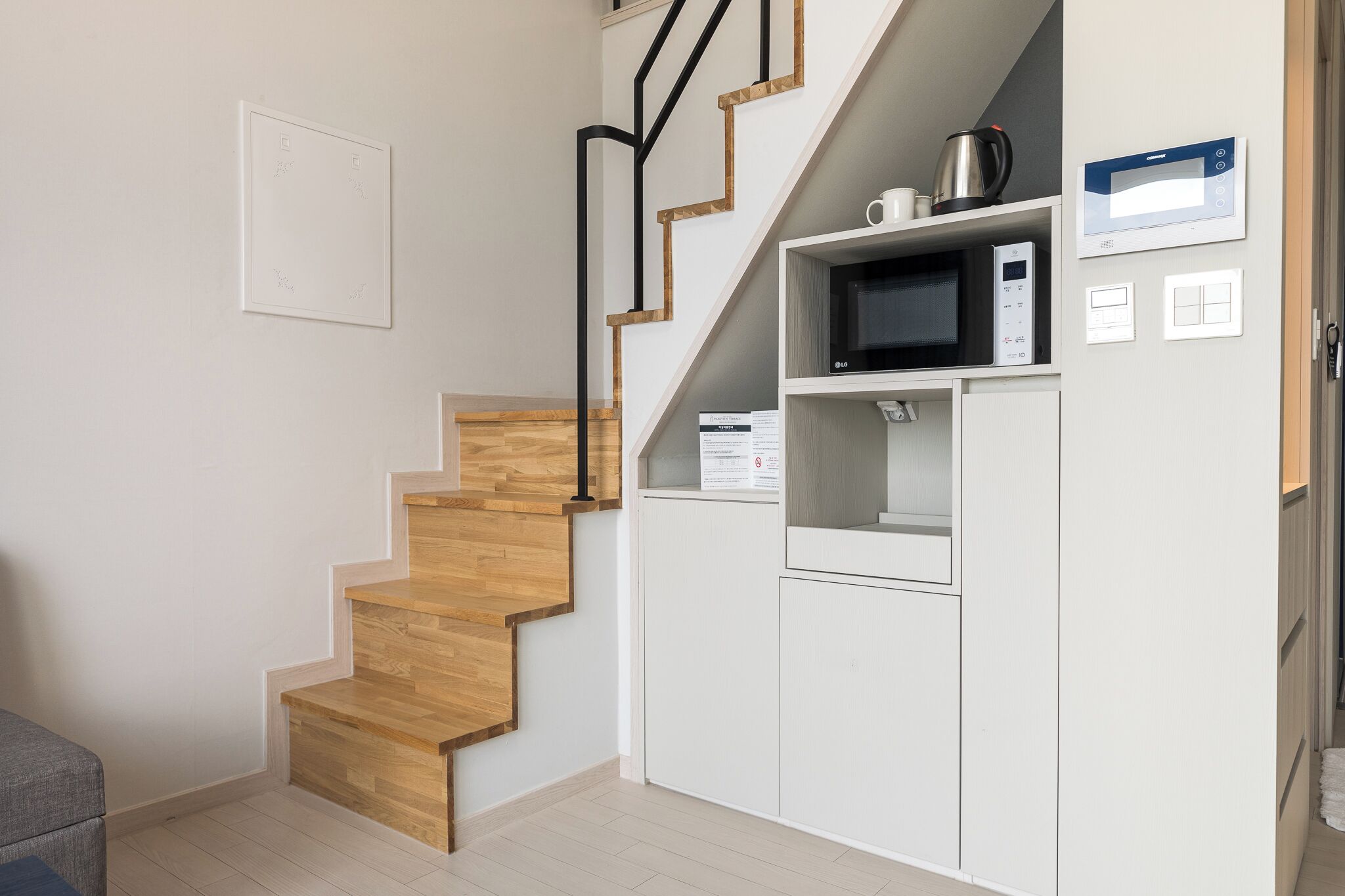 A modern kitchen with a wooden staircase, built-in microwave, and white cabinetry.