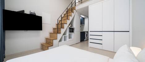 Un dormitorio moderno con una cama grande, un armario empotrado, una escalera que lleva a una cocina y un televisor de pantalla plana montado en la pared.