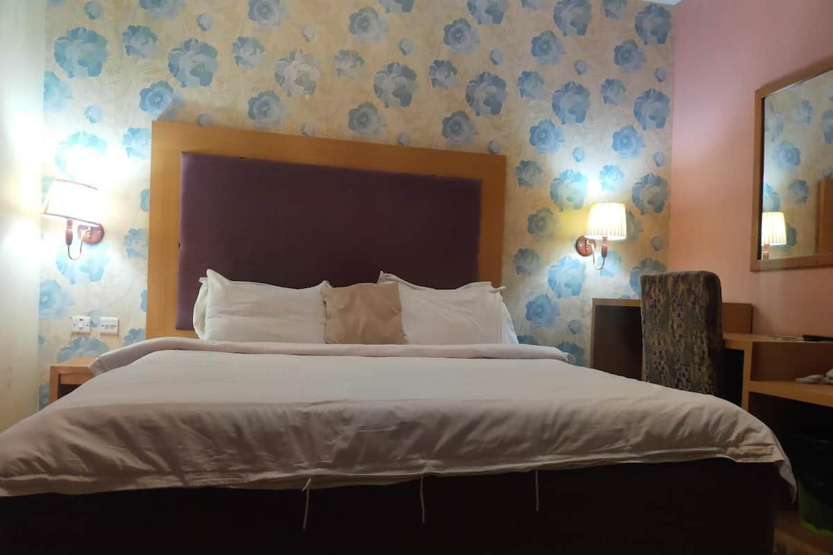 A hotel room with a large bed, a wooden headboard, two wall-mounted lamps, and a floral wallpaper pattern.