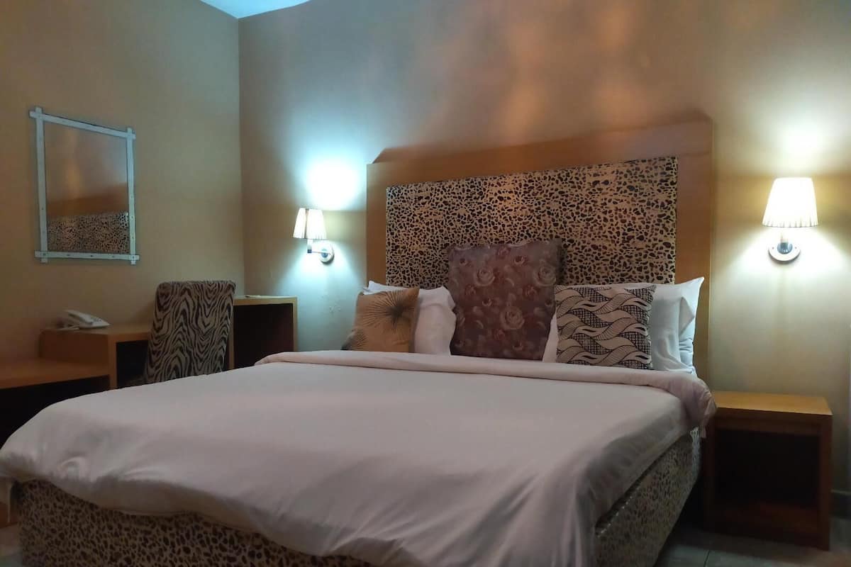 A hotel room with a large bed, two bedside tables, a chair, a mirror, and two wall-mounted lamps.