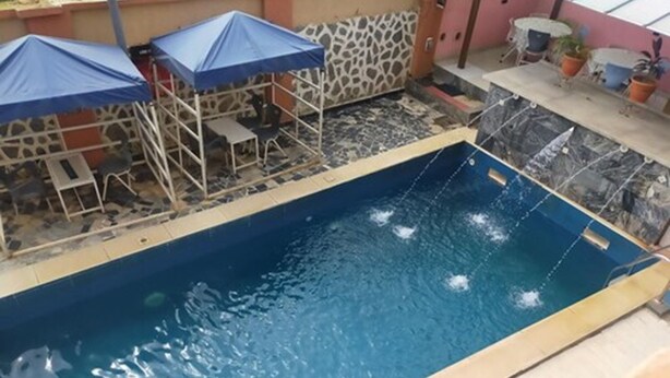 Ein Schwimmbecken mit gefliestem Sonnendeck, blauen Sonnenschirmen und einem kleinen Tisch mit Stühlen.