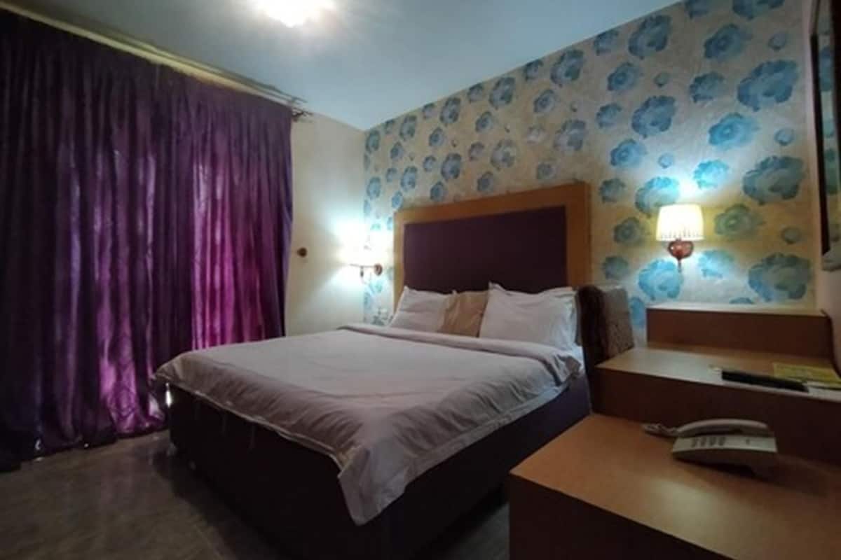 A hotel room with a bed, a nightstand, a telephone, and a wall with floral wallpaper.