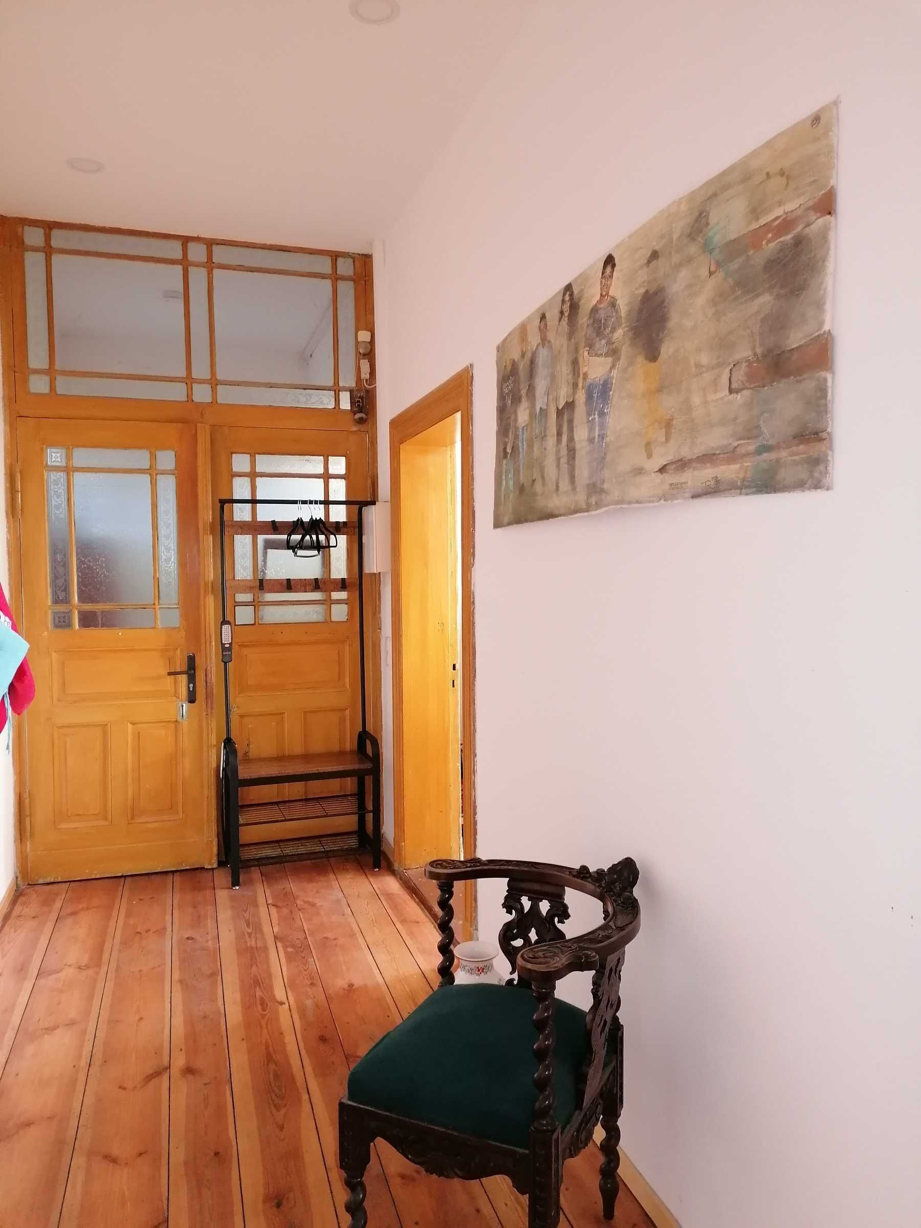 Une pièce avec un plancher en bois, une porte en bois dotée de panneaux de verre, un banc et un tableau accroché au mur.