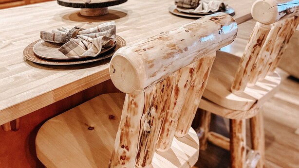 Uma mesa de jantar de madeira com design rústico, rodeada por cadeiras de madeira com acabamento natural.