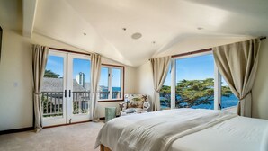 A bedroom with a large bed, a view of the sea, and a balcony with a railing. - Seafarer - Pacific Grove Beach House - Steps to the Water, Incredible Ocean Views (Pacific Grove)