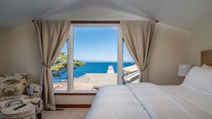 A bedroom with a large window, a bed, a nightstand, and a view of the sea. - Seafarer - Pacific Grove Beach House - Steps to the Water, Incredible Ocean Views (Pacific Grove)