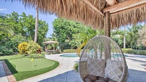 A hanging chair with cushions, a small pool, and a well-maintained garden with a putting green.