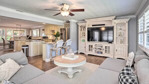 A spacious living room with a round table, a sofa, and a television in a well-lit kitchen area with cabinets and a ceiling fan.
