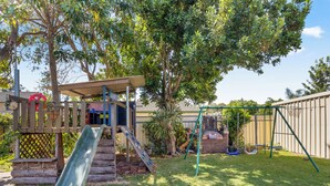 Un jardin avec une aire de jeux en bois, un four en briques et une balançoire.