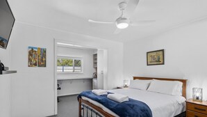 Une chambre à coucher avec un lit, un ventilateur de plafond, une fenêtre et des œuvres d’art accrochées aux murs.