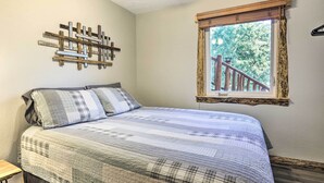 A bedroom with a bed, a wooden headboard, a window with a view of a wooden deck, and a wall-mounted wooden art piece. - Spacious Black Hawk Home w/ Furnished Deck! (Black Hawk)