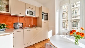 A modern kitchen with white cabinets, a microwave, and an oven. There is a dining table with a vase of flowers. - Co-ownership (Nice)