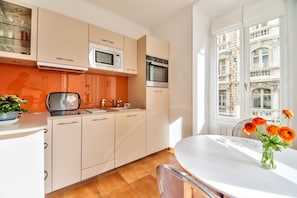 A modern kitchen with white cabinets, a microwave, and an oven. There is a dining table with a vase of flowers.