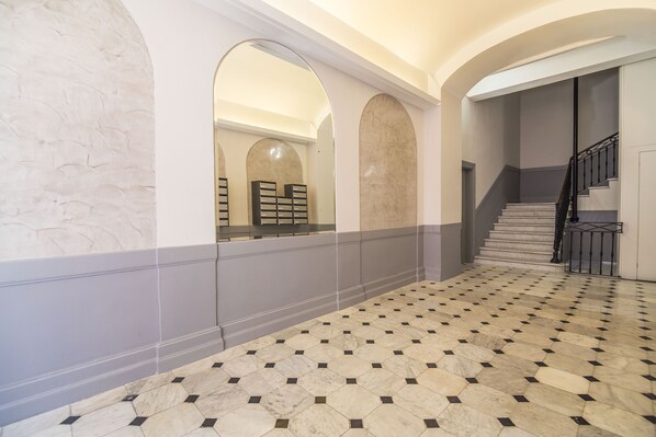 A spacious hallway with a patterned floor, a staircase, and arched doorways leading to another area.